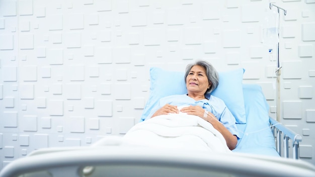 写真 病気の症状に疲れて病室で生理食塩水を受けてベッドに横たわっている年配の女性患者