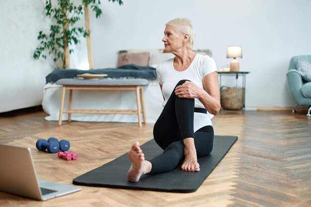 Elderly woman performing pilates gymnastics online in her living room concept of a healthy lifestyle