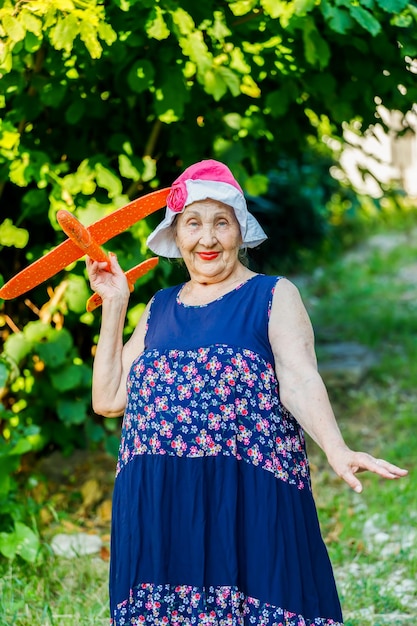 An elderly woman plays with a toy airplane in the garden in the summer