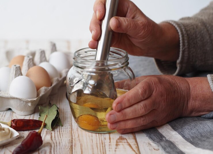 Photo an elderly woman prepares homemade mayonnaise in a jar with vegetable oil and an egg