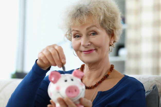 An elderly woman puts a coin in a piggy bank