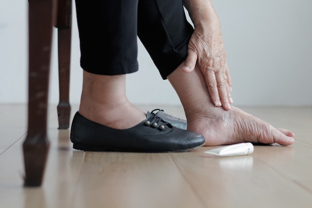 Elderly woman putting cream on swollen feet before put on shoes