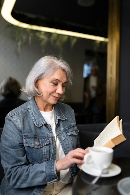 写真 本を読んで、カフェでコーヒーを飲む年配の女性