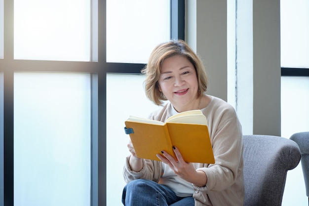 커피 한잔과 함께 편안한 하루에 창에 의해 책을 읽고 노인 여성.