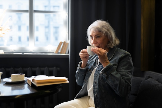 Foto donna anziana che legge un libro e beve caffè in un bar