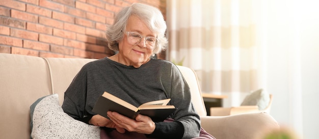 Elderly woman reading book on sofa in living room Banner design