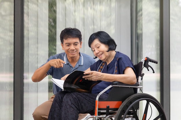 車椅子で息子と一緒に本を読んでいる年配の女性が世話をします。