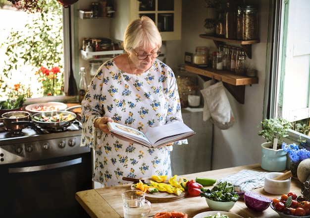 Photo elderly woman reading a cookbook in the kitchen