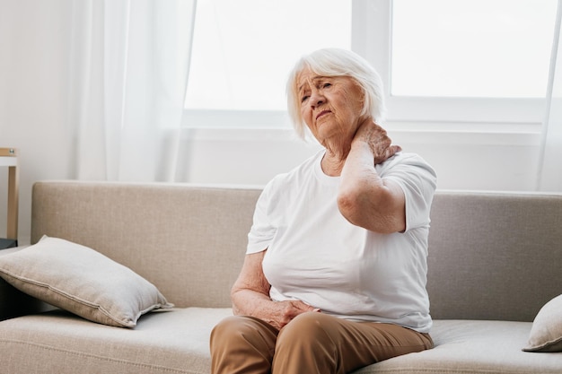 Elderly woman severe neck pain sitting on the sofa health problems in old age poor quality of life