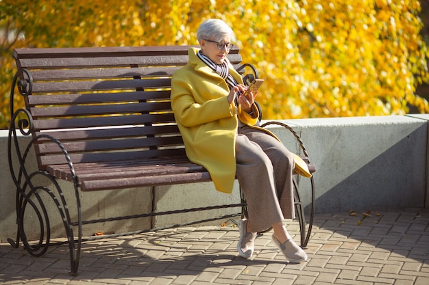 elderly woman sits on a bench with a phone