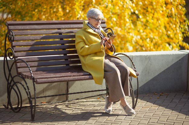 elderly woman sits on a bench with a phone