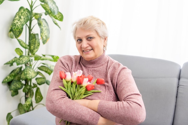 年配の女性は、チューリップの花束とソファに座っています。母の日。