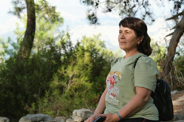 Elderly woman sits on a stone and rests during a hiking trip