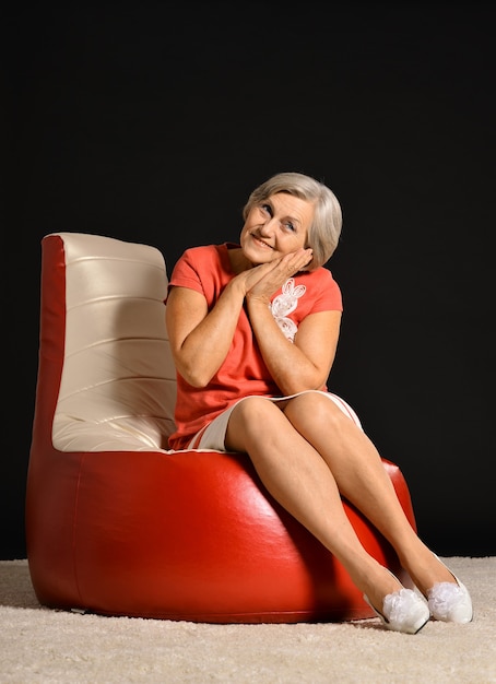 Elderly woman sitting on red armchair in dark studio