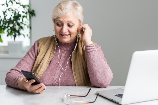 Elderly woman sitting at table typing on a smartphone.