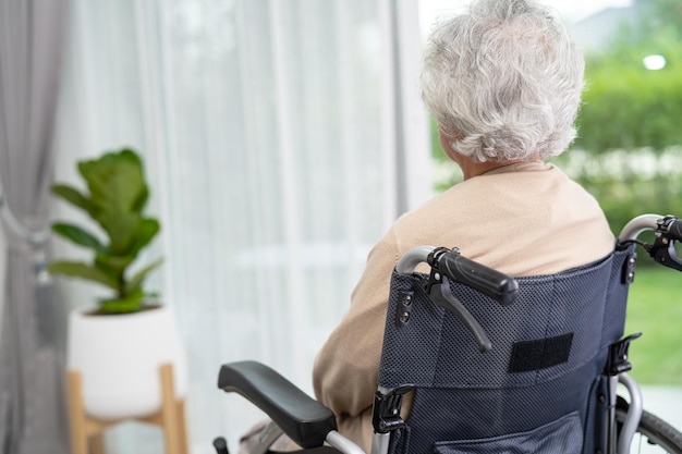 An elderly woman sitting on wheelchair looking out the window for waiting someone Sadly melancholy and depressed