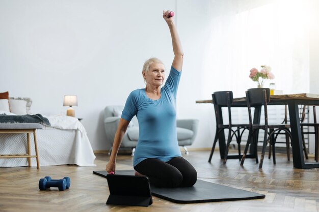 Photo elderly woman sitting in a yoga pose in front of an open laptop