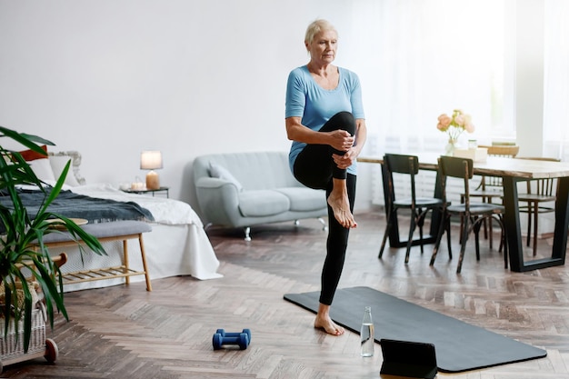 Elderly woman sitting in a yoga pose in front of an open laptop