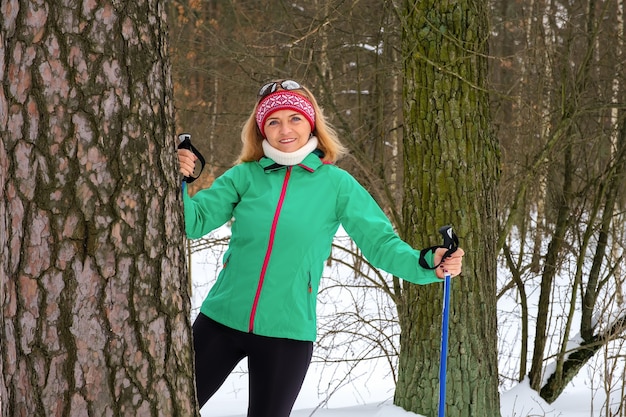 写真 冬の森でノルディックウォーキングポールと立っている年配の女性