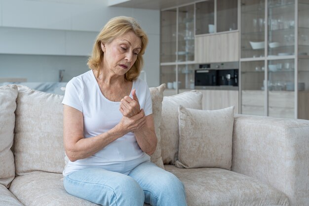 ソファに座っている手の関節炎に苦しんでいる年配の女性精神の概念