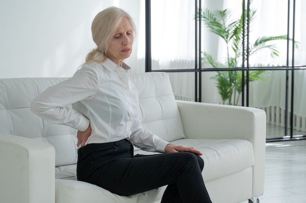 허리 통증으로 고통받는 노인 여성 중년 여성이 소파에서 일어나 허리 통증을 경험합니다
