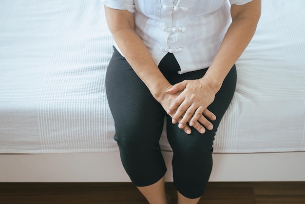 침실에 앉아 다리와 무릎 부상으로 고통받는 노인 여성