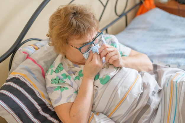 An elderly woman suffers from the flu and runny nose The pensioner blows her nose in the nasal raft