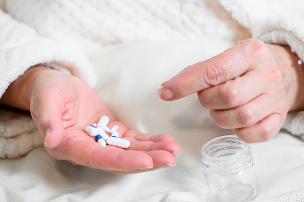 Elderly woman taking medicines, picking pills from hand, closeup view.