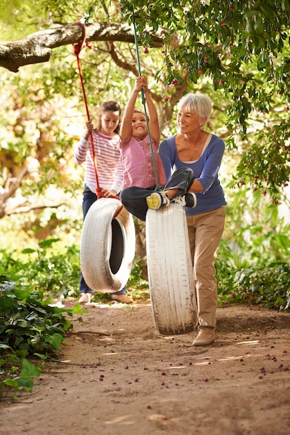 Elderly woman tire swing and grandma playing with grandkids or holidays and having fun in a garden in summer Excited grandchildren and outdoors swinging together or on sunny weekend at a park