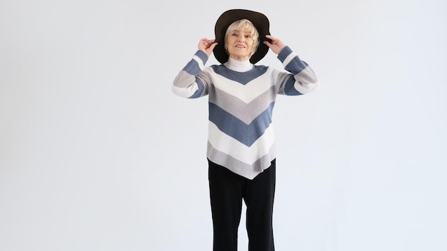 An elderly woman tries on a hat on a white background