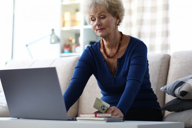 Пожилая женщина использует банковскую карту для оплаты онлайн.