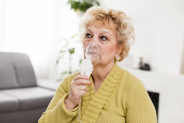 Elderly woman using asthma machine on light background