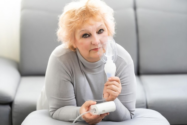 Elderly woman using asthma machine on light background.