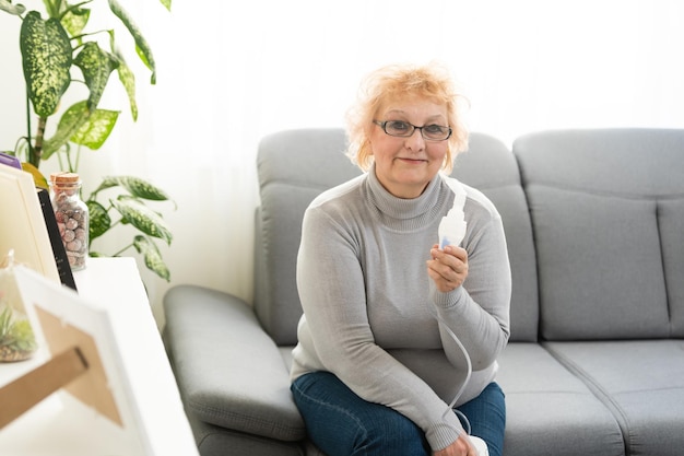 Elderly woman using asthma machine on light background.