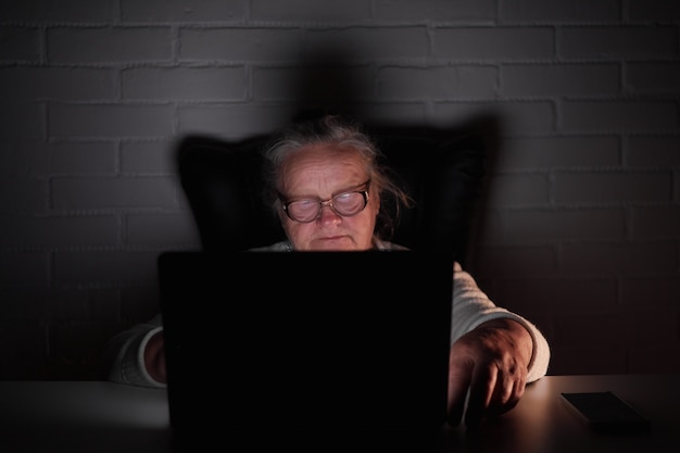 暗闇の中でノートパソコンを使用している年配の女性