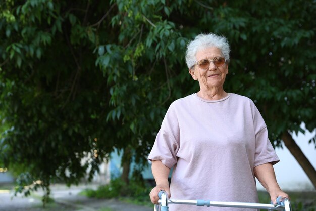 Elderly woman using walking frame in park Space for text