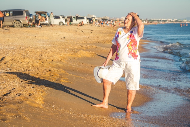 年配の女性が海岸沿いを歩いています。海での夏休み。