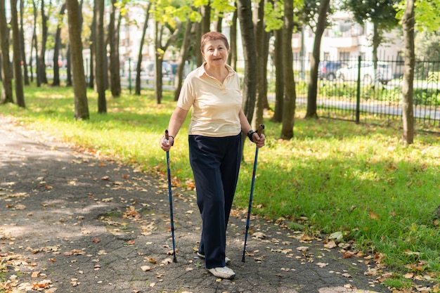 An elderly woman walks nordic with sticks in the park on a sunny summer day