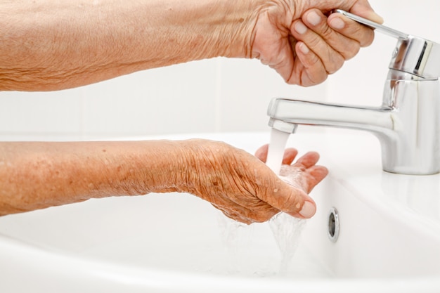 Elderly woman washes hand in bathroom