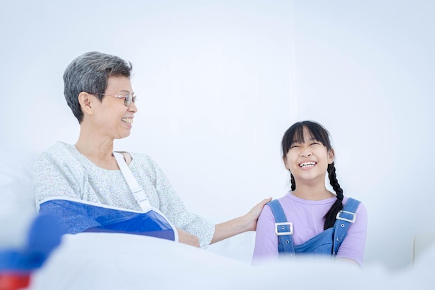 Elderly woman wear arm splint with her granddaughter having fun talking at hospital Medical treatment health insurance concept