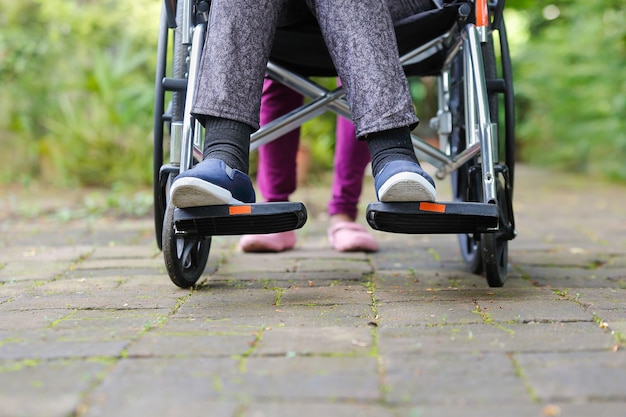 Elderly woman in wheelchair walking with caregiver