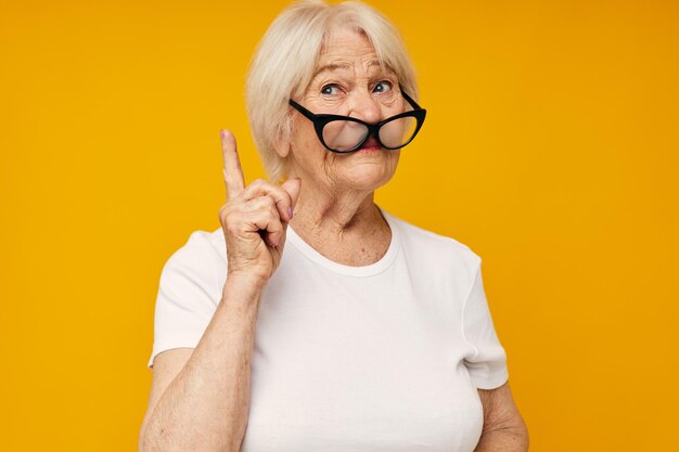 Elderly woman in a white tshirt wears glasses yellow background