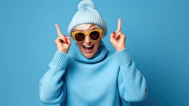 Elderly woman in winter hat and sweater pointing fingers up on blue background
