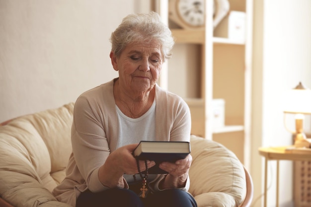 Elderly woman with Bible and rosary beads at home