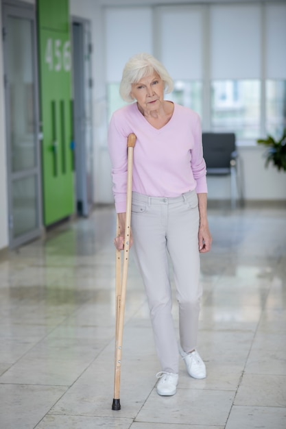 Пожилая женщина с костылем идет по коридору