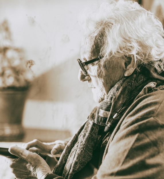 Elderly woman with glasses looking at mobile phone at home.