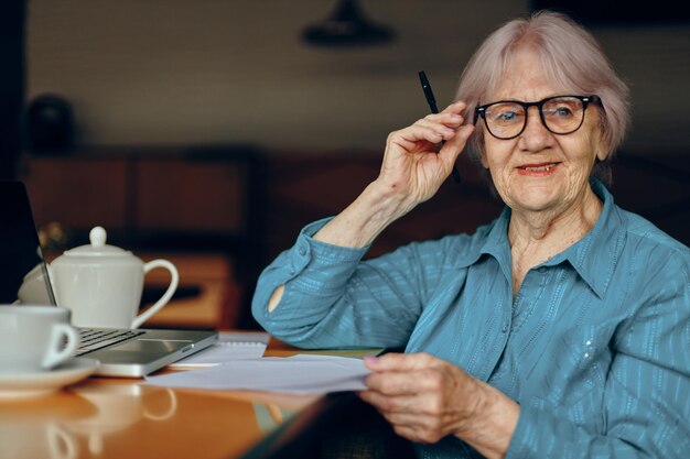 Elderly woman with glasses sits at a table in front of a laptop Freelancer works unaltered