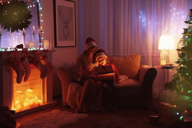 Пожилая женщина с внуком открывает рождественский подарок, сидя на диване в гостиной