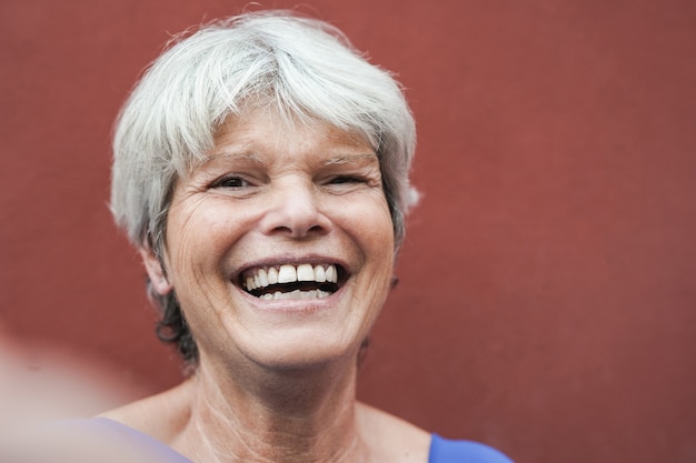 Foto donna anziana con i capelli grigi che si fa un selfie usando il telefono cellulare - la persona anziana gode della tecnologia