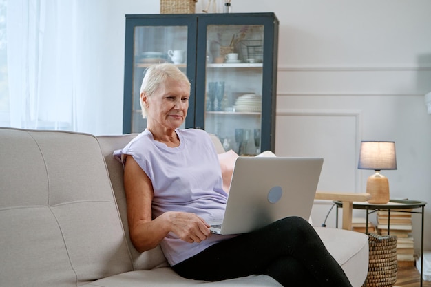 ラップトップを持つ年配の女性は、居間で自由な時間を過ごしています